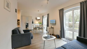 A modern living room with a sofa, a coffee table, and a dining area with a table and chairs. - Comfortable, modern living in a central, quiet island location for 2 people (Wangerooge)