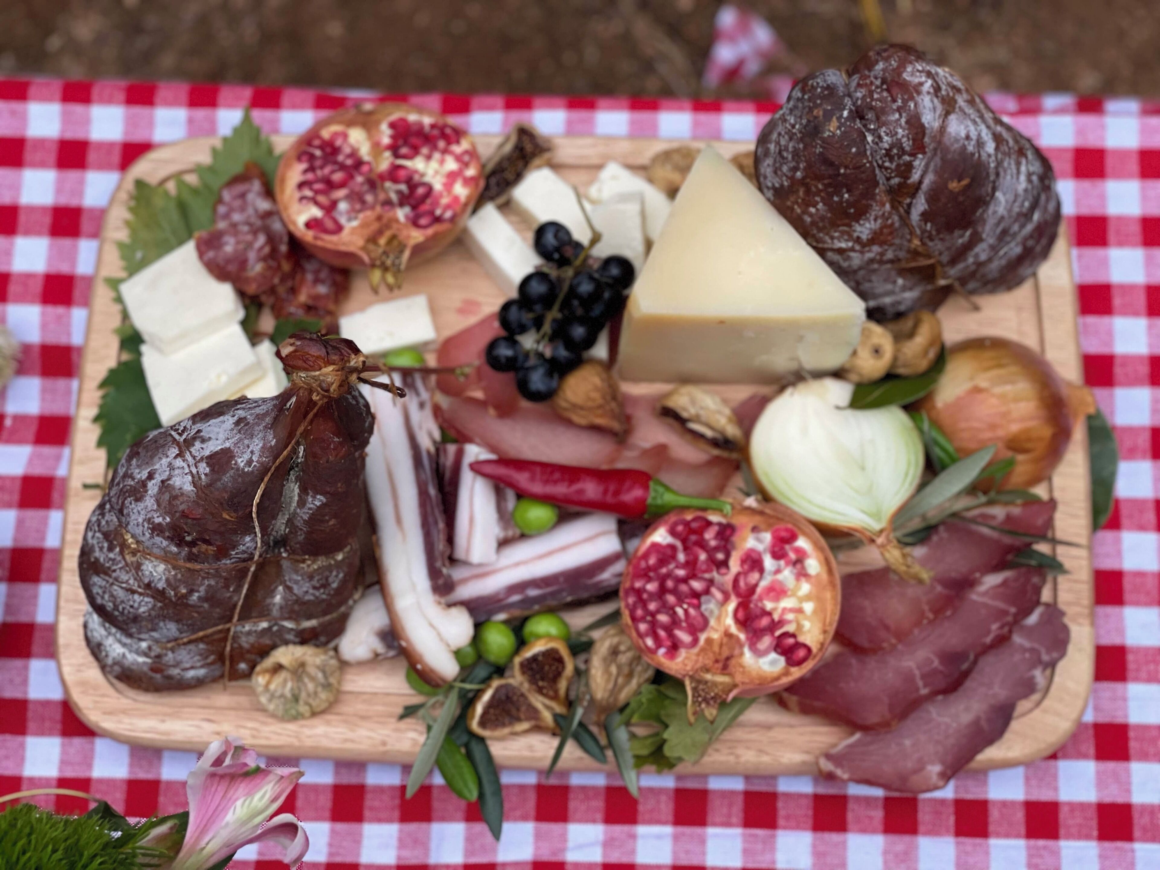 Een charcuterieplank met verschillende vleessoorten, kazen, fruit en noten op een houten plank.