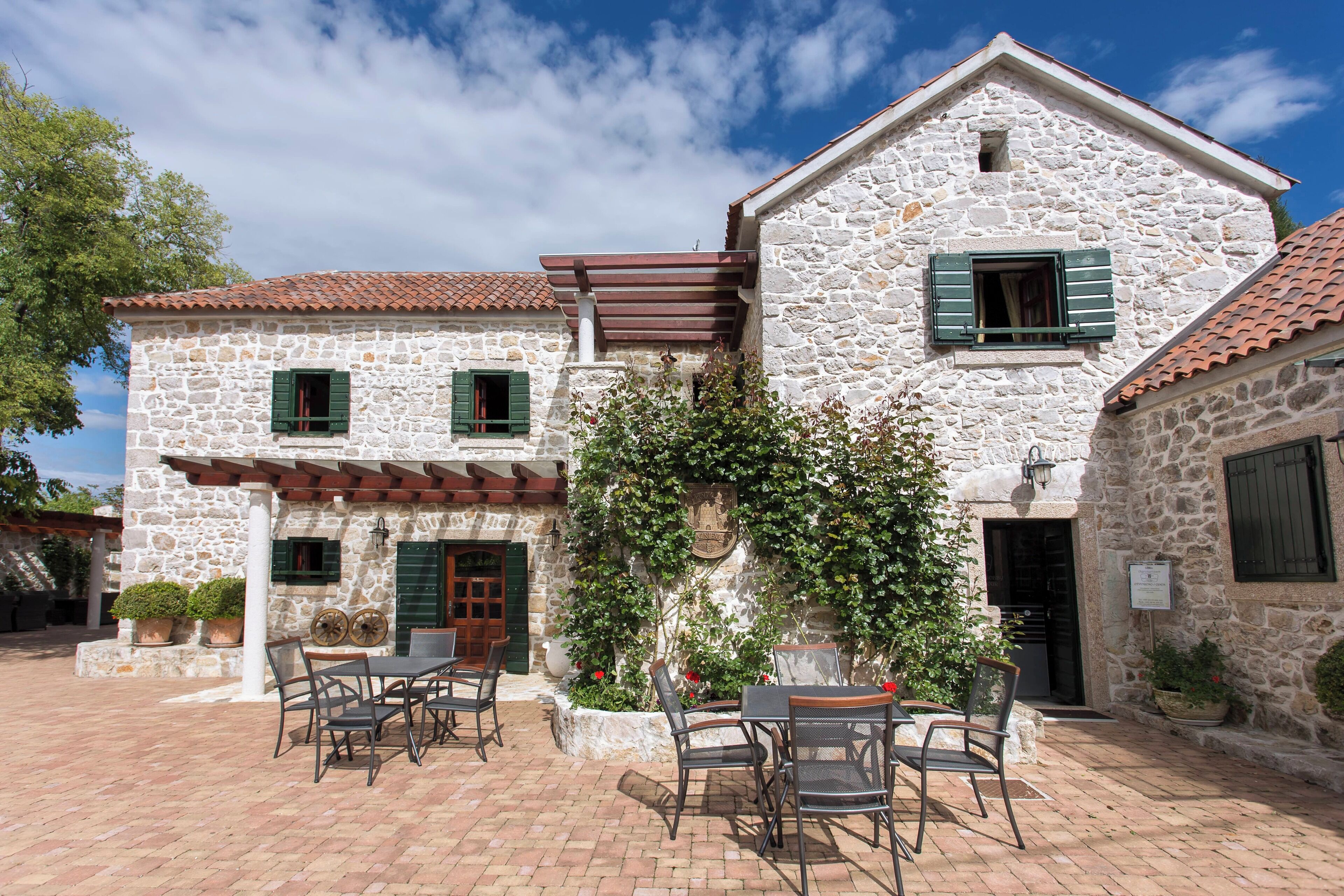 A stone building with a tiled roof, outdoor seating, and potted plants.
