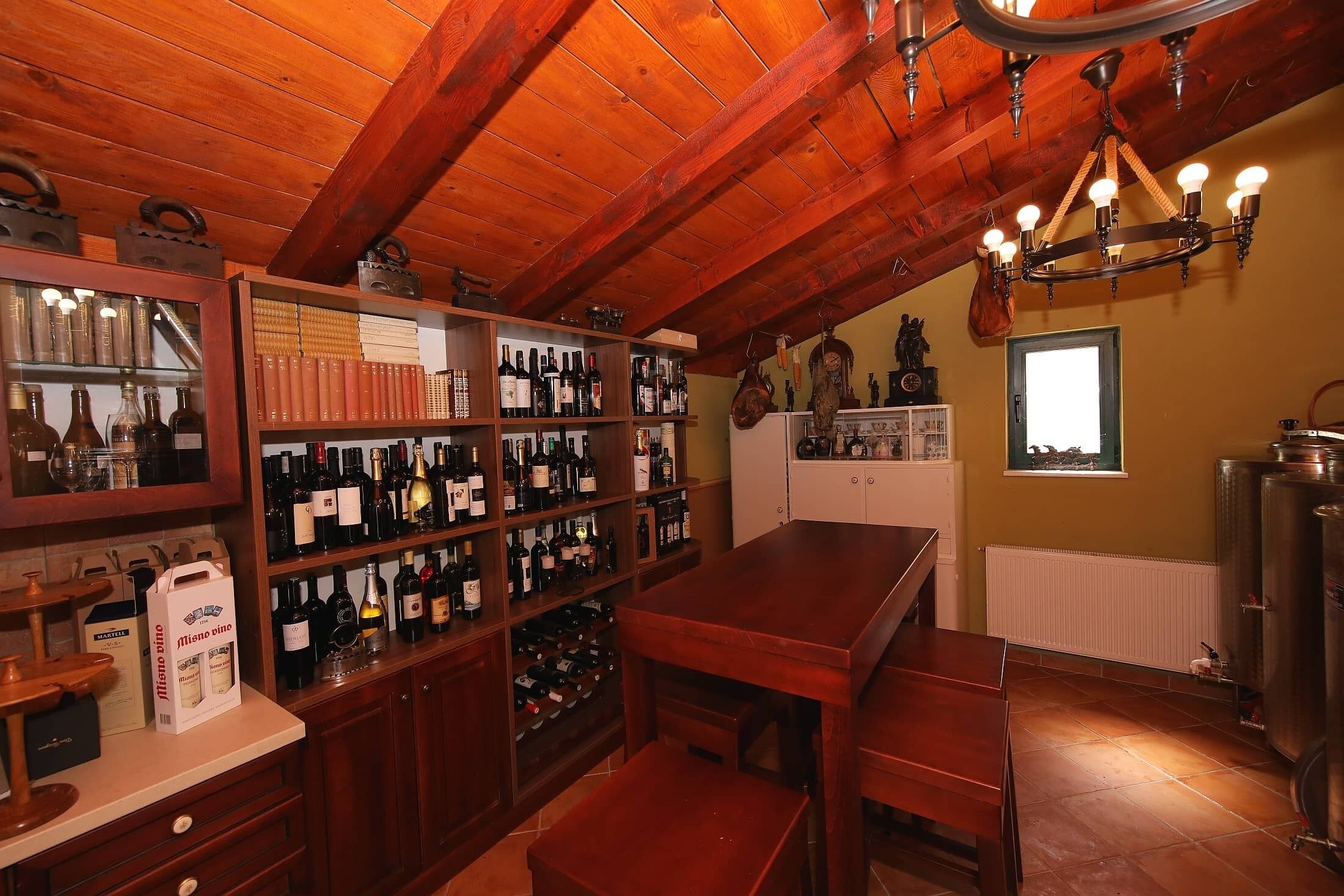 A rustic cellar with wooden beams, wine racks, and a wooden table.