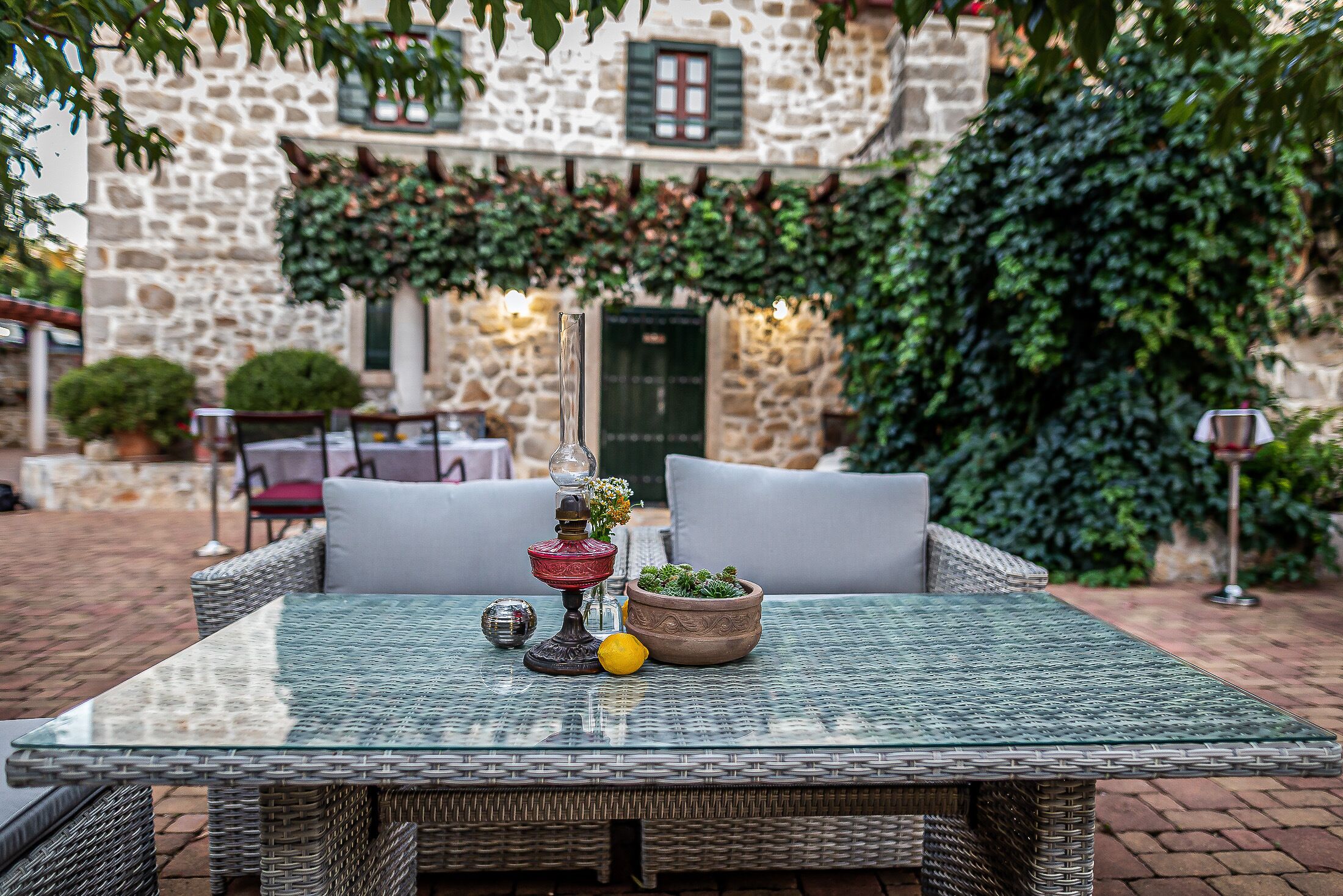 An outdoor seating area with wicker furniture, a glass table, and a potted plant.