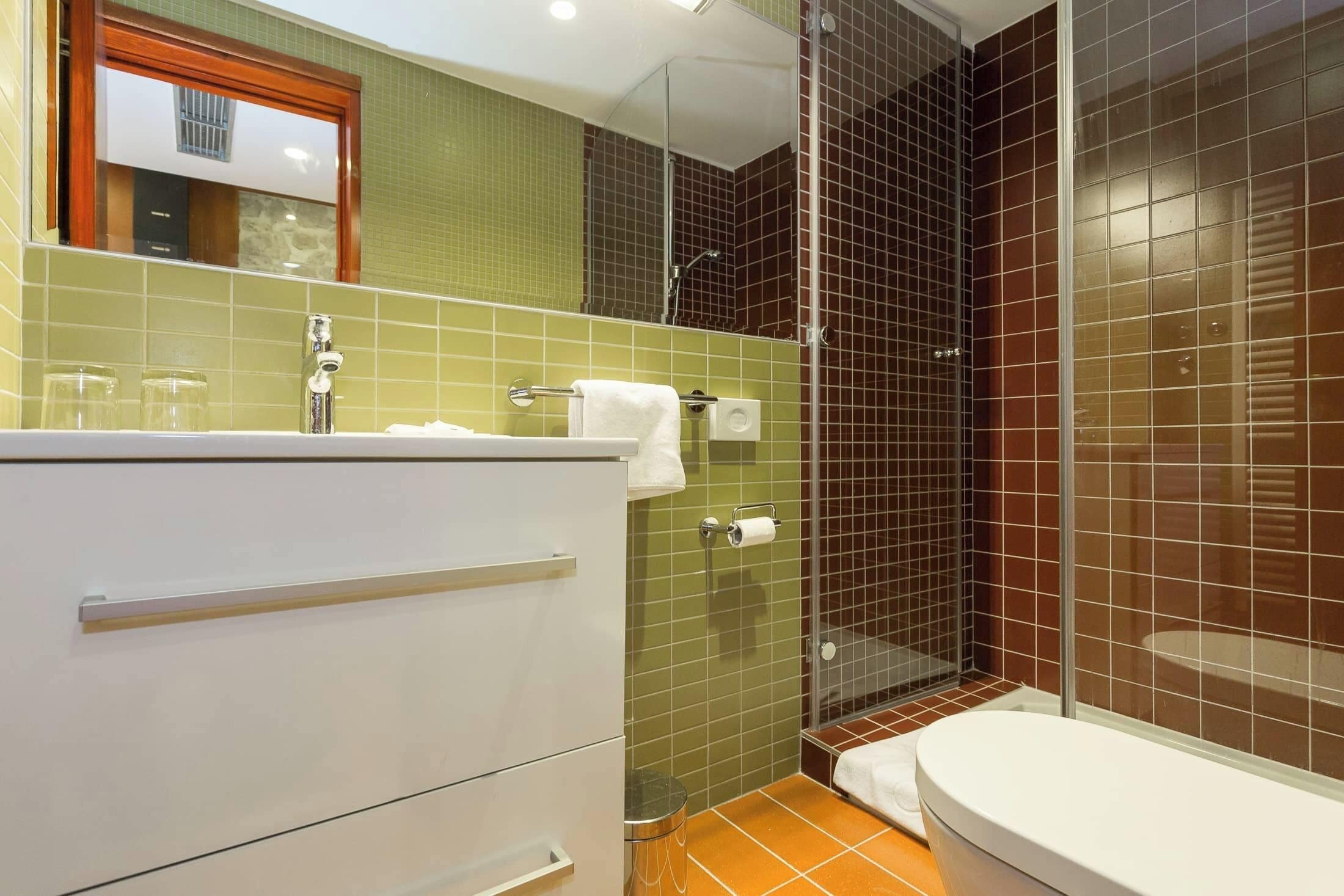 Un baño con tocador blanco, cabina de ducha de vidrio y retrete.