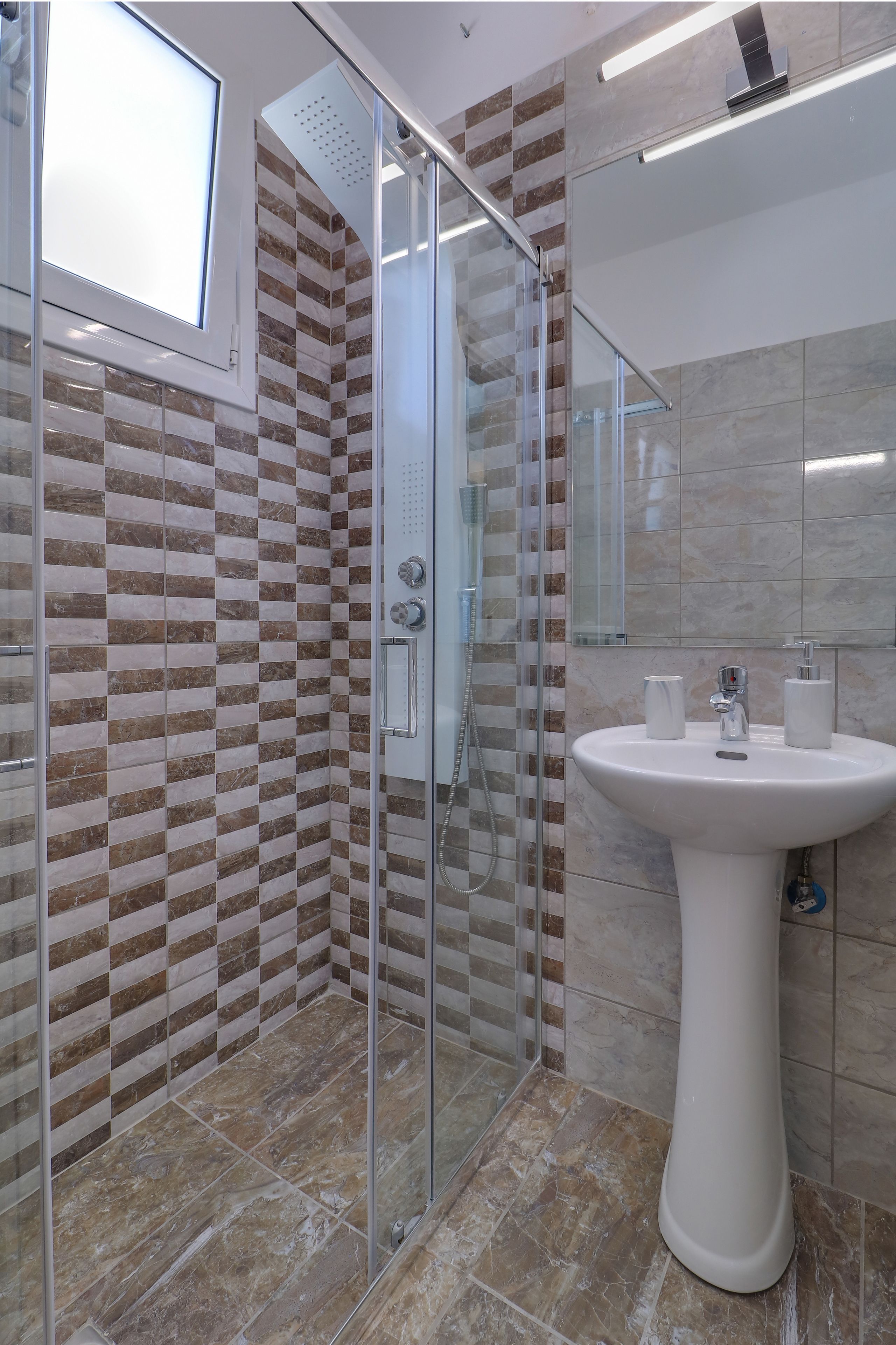 Un baño con cabina de ducha de vidrio, un lavabo blanco y una pared de azulejos con diseño a cuadros.