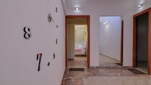 A hallway with numbered doors, a tiled floor, and a view into a bedroom with a bed and a radiator. - Carpe Diem Apartments By Athens Airport (Markopoulo Mesogaias)
