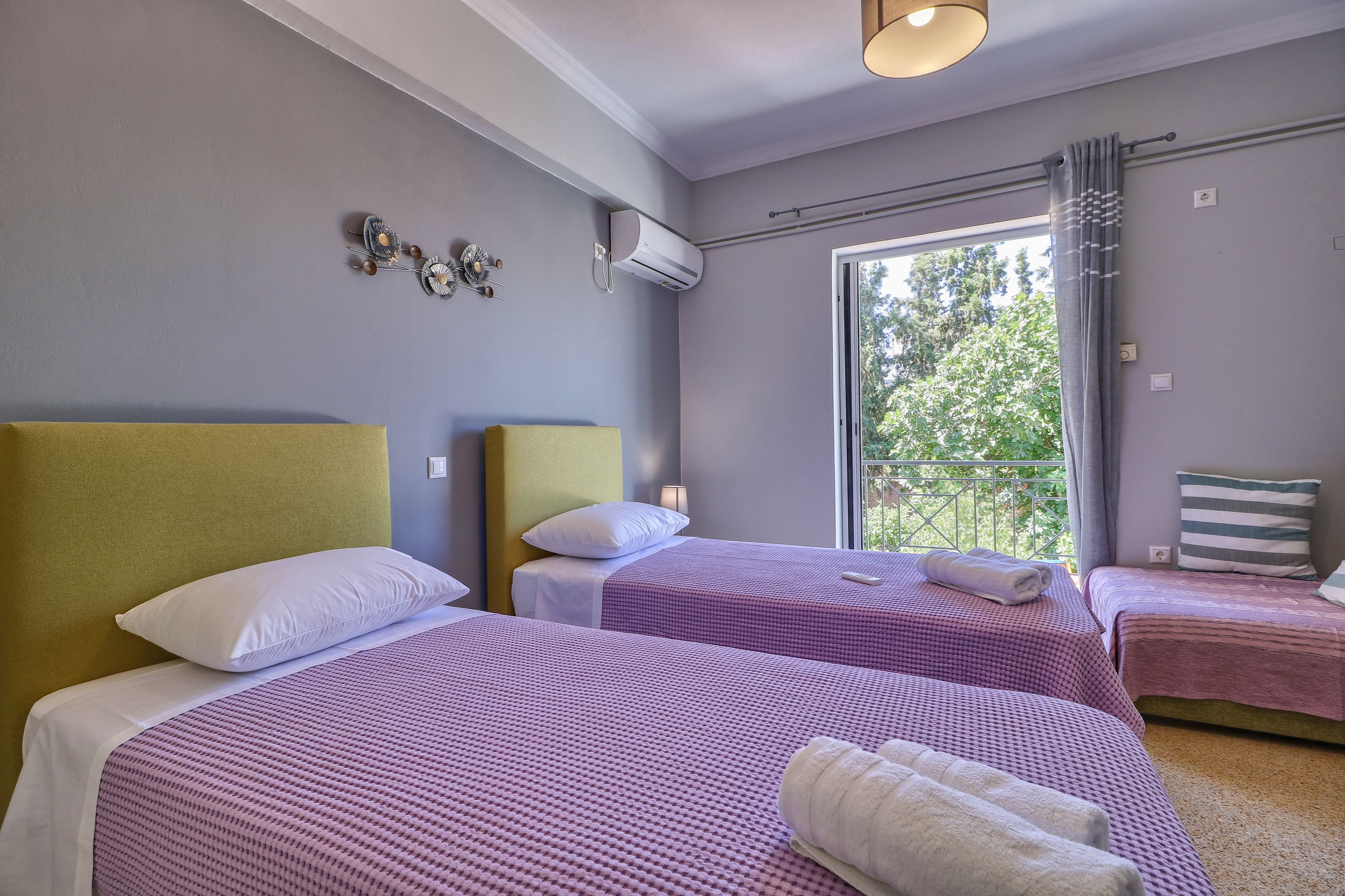 Habitación de hotel con dos camas, una ventana con vista a árboles y un equipo de aire acondicionado en la pared.