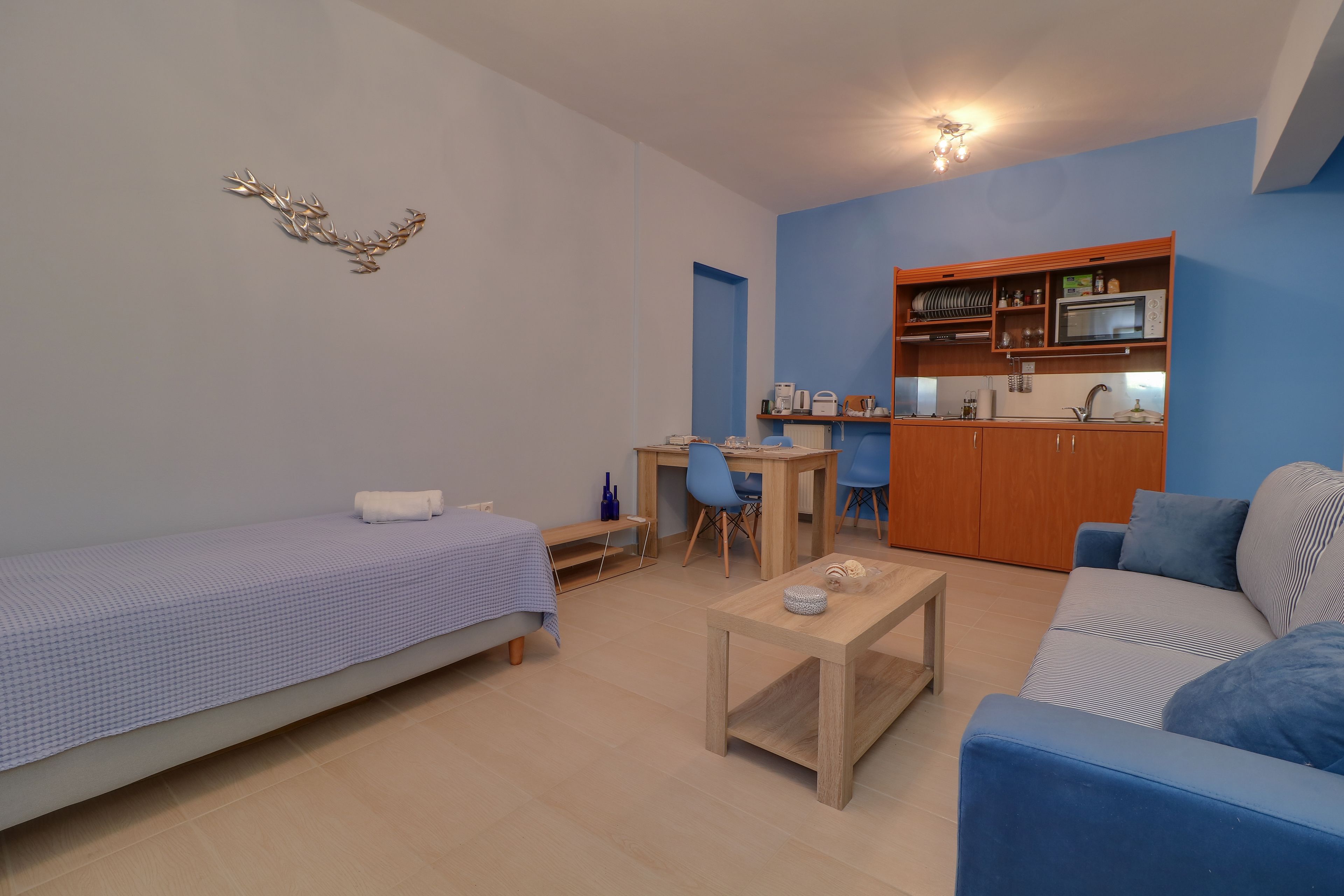 Un espacio habitable compacto con una cama individual, un sofá, una mesita, una kitchenette y un área de comedor.