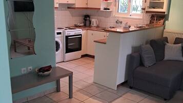 A compact kitchen with a stove, oven, and sink, a dining area with a bench, and a sofa.