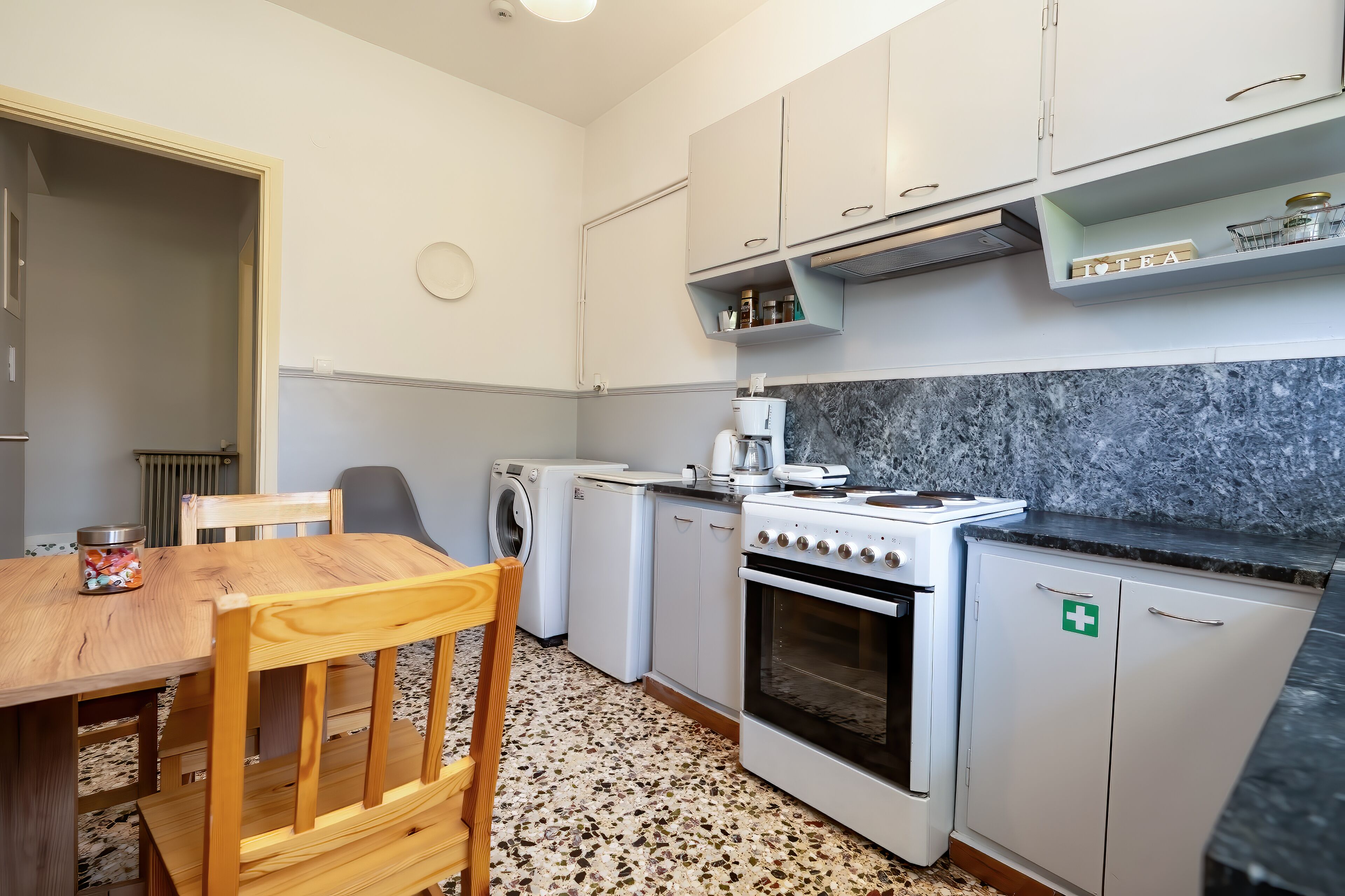 A compact kitchen with a stove, oven, and a coffee maker. There is a wooden dining table with chairs.