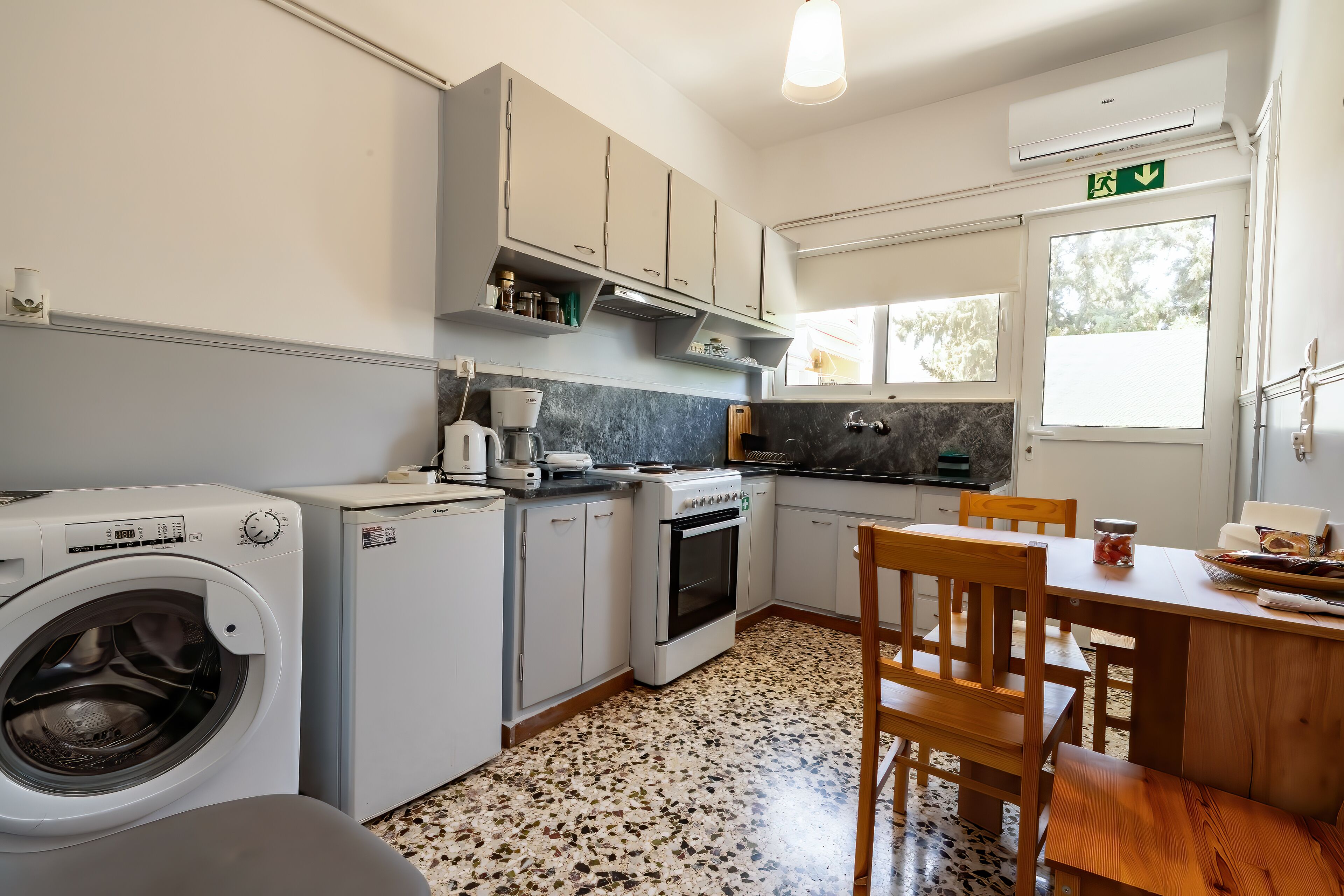 Une cuisine compacte équipée d’un lave-linge, d’une machine à café et d’un coin repas avec une table et des chaises.