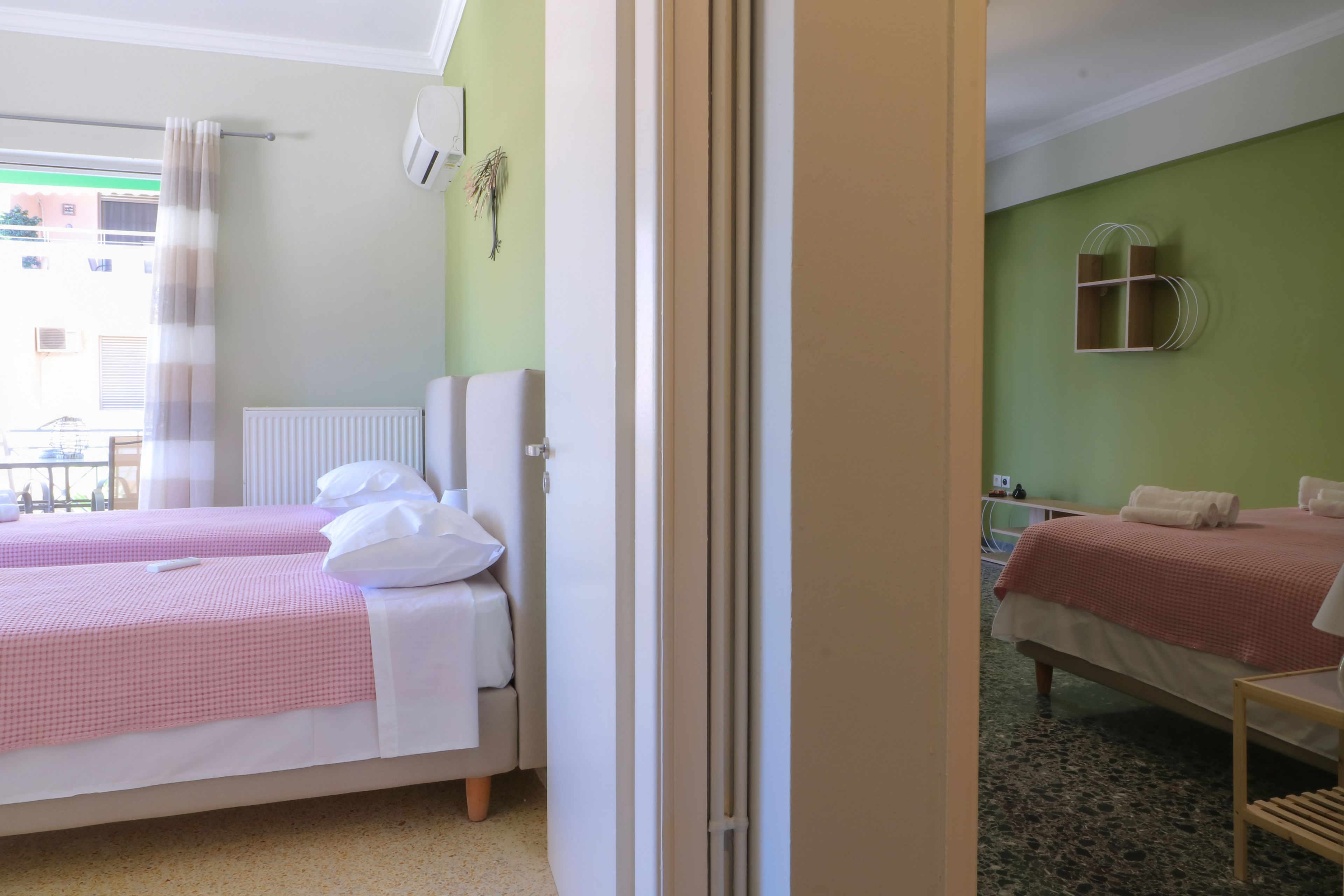 Hotelkamer met twee bedden, een radiator, een raam met gordijnen, een wandairconditioner en een tafeltje met een stoel.
