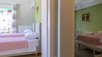 Habitación de hotel con dos camas, un radiador, una ventana con cortinas, un aire acondicionado montado en la pared y una mesita con una silla.