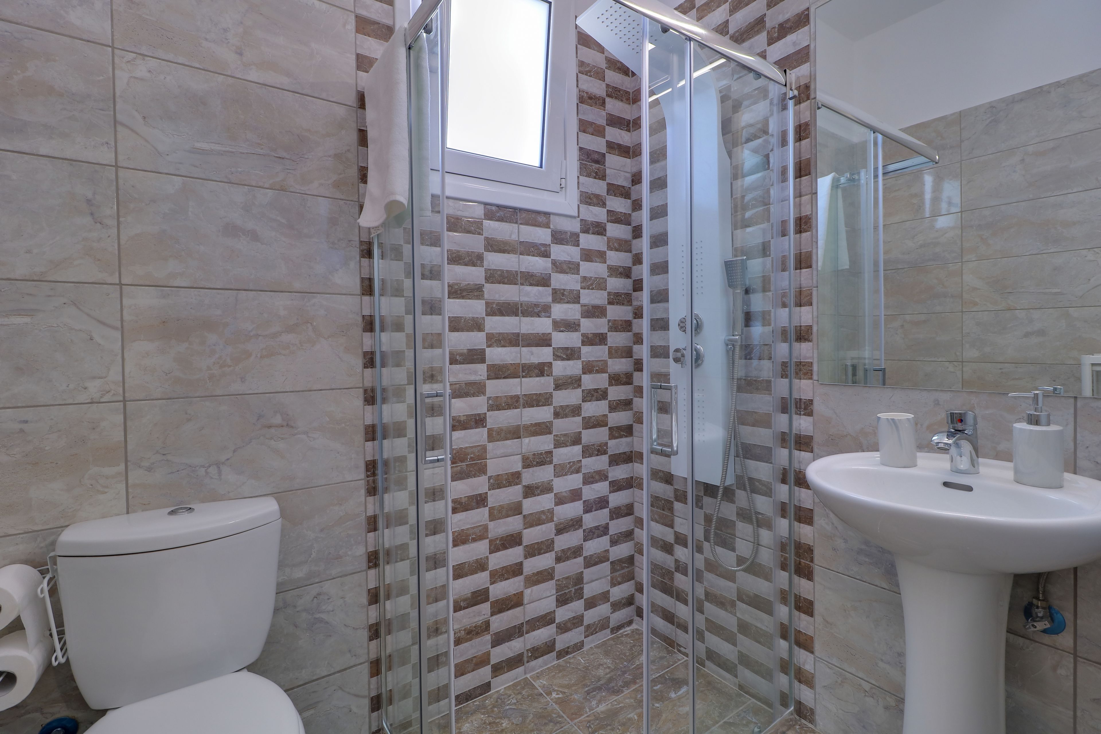 Un baño con ducha envuelta en vidrio, inodoro y lavamanos con espejo.
