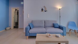 A living room with a blue sofa, a wooden coffee table, and a floor lamp. - Carpe Diem Apartments By Athens Airport (Markopoulo Mesogaias)