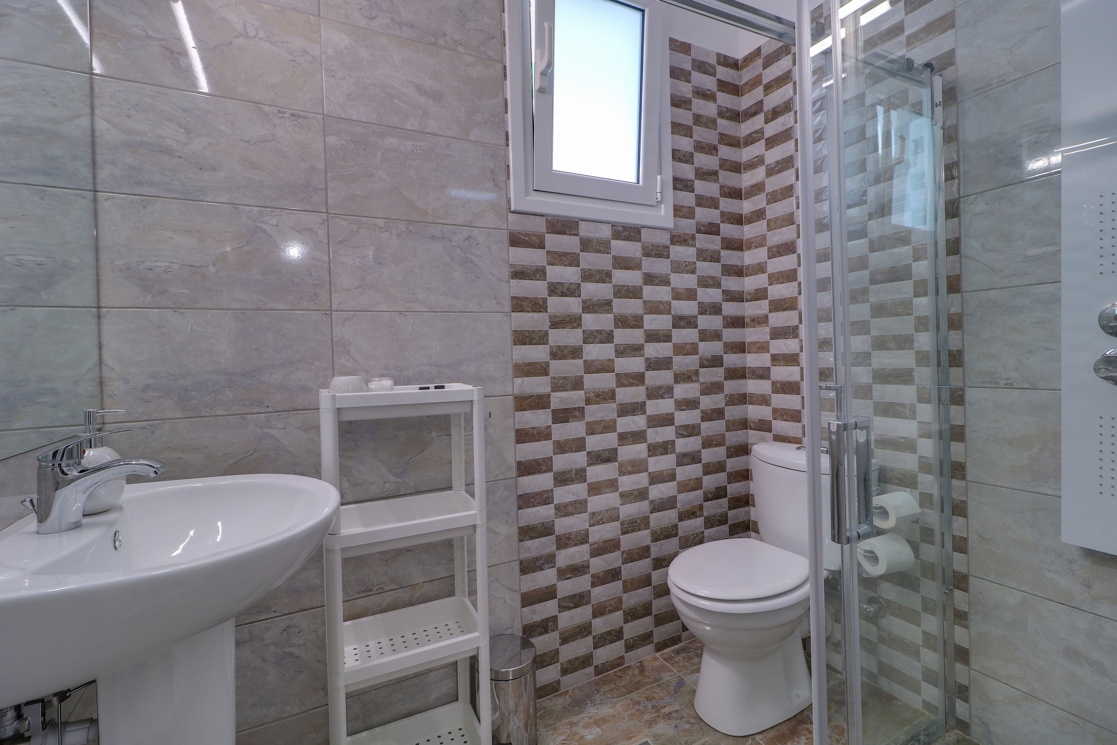 Un baño con lavamanos, inodoro y cabina de ducha con mampara de vidrio.