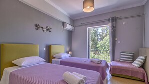 A hotel room with two beds, a window with a view of trees, an air conditioning unit, and a ceiling light. - Carpe Diem Apartments By Athens Airport (Markopoulo Mesogaias)