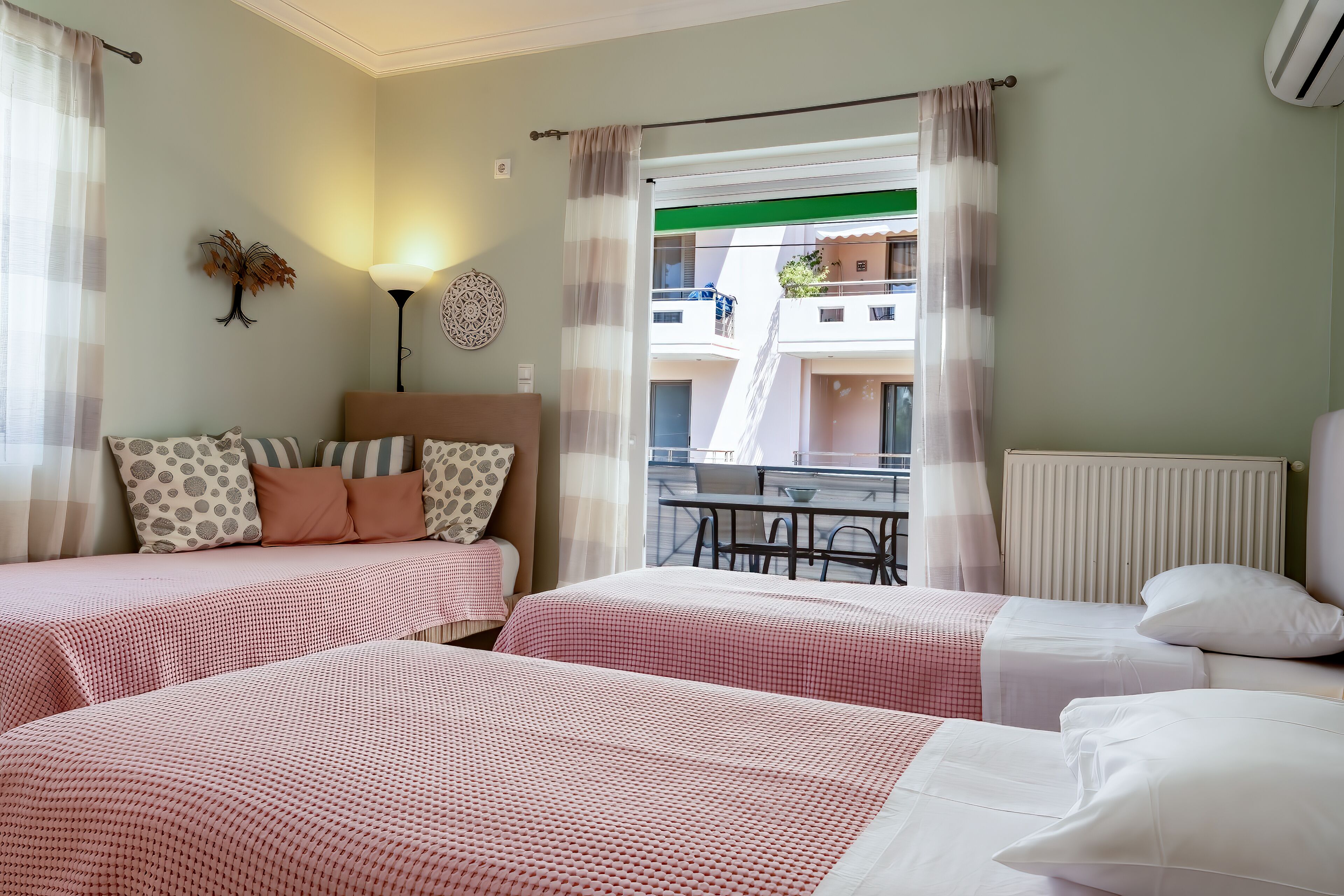 Quarto de hotel com duas camas, uma mesa, cadeiras, um abajur e vista para edifícios pela janela.