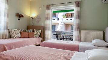 Quarto de hotel com duas camas, uma mesa, cadeiras, um abajur e vista para edifícios pela janela.