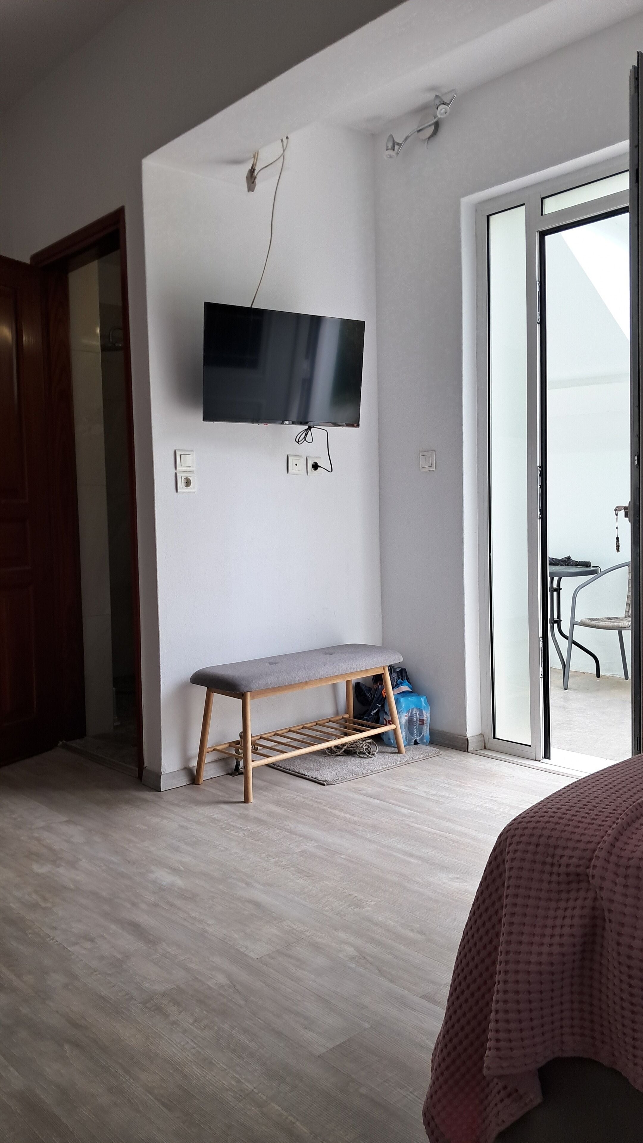 Una habitación con un banco de madera, un televisor de pantalla plana montado en la pared, un ventanal corredero que da a un espacio exterior y una puerta de madera.
