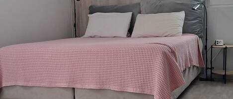 A bedroom with a bed, a bedside table, a lamp, and a window.