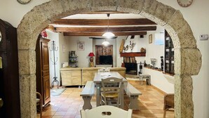 A rustic interior with a stone archway leading to a dining area, a fireplace, and a television. - Gîte La Ferme de Cabanis de Labahou SPA 8 pers (Anduze)