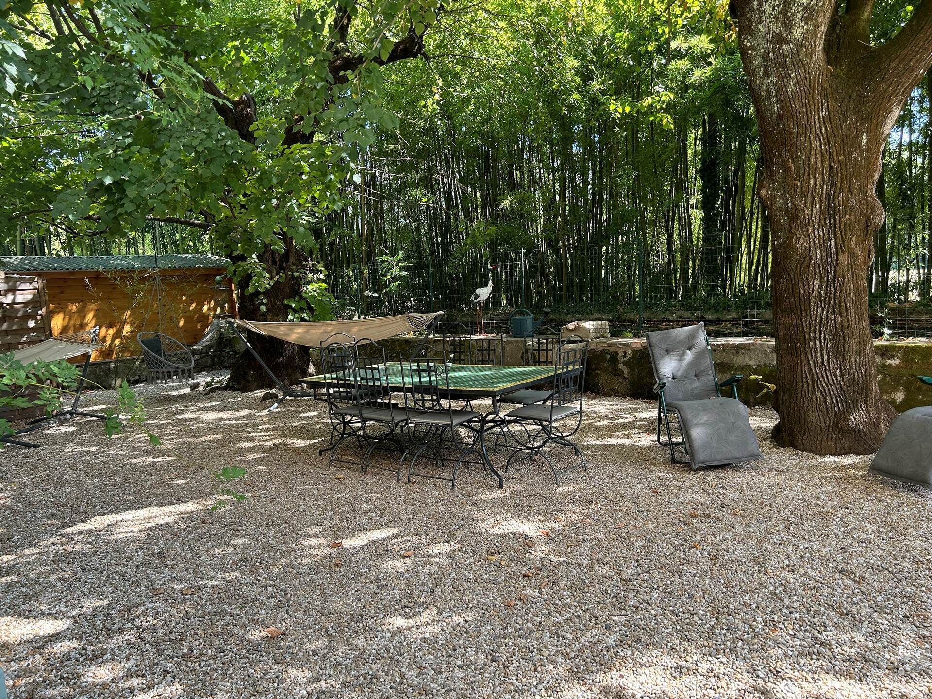 Un espace extérieur aménagé dans un style rustique, avec une table et des chaises, entouré d’arbres et d’une structure en bois.
