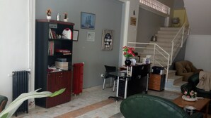 A spacious living room with a green sofa, a coffee table, and a bookshelf. A staircase is visible in the background leading to an upper level. - Remes hotel (Constantine)