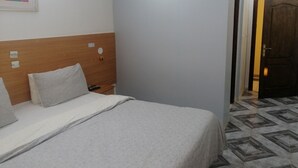 A hotel room with a bed, a wooden headboard, a nightstand, and a door. - Remes hotel (Constantine)