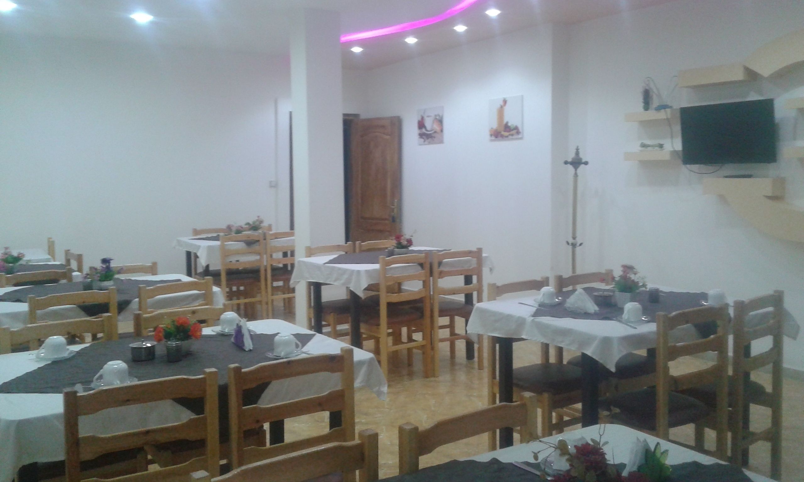 A dining area with multiple tables and chairs, a wooden door, and a television mounted on the wall.
