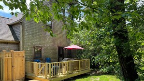 A wooden deck with a red umbrella, a small outdoor seating area, and a stone building with a window. - 2 Bed/2 Bath on 1/4 acre w/fenced yard, short walk to 40th thru rolling dunes. (Nantucket)