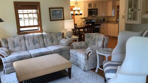 A living room with a sectional sofa, a round coffee table, and a white armchair. - 2 Bed/2 Bath on 1/4 acre w/fenced yard, short walk to 40th thru rolling dunes. (Nantucket)