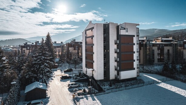 Un edificio moderno de varios pisos con un patio central, rodeado de árboles cubiertos de nieve y un paisaje montañoso.