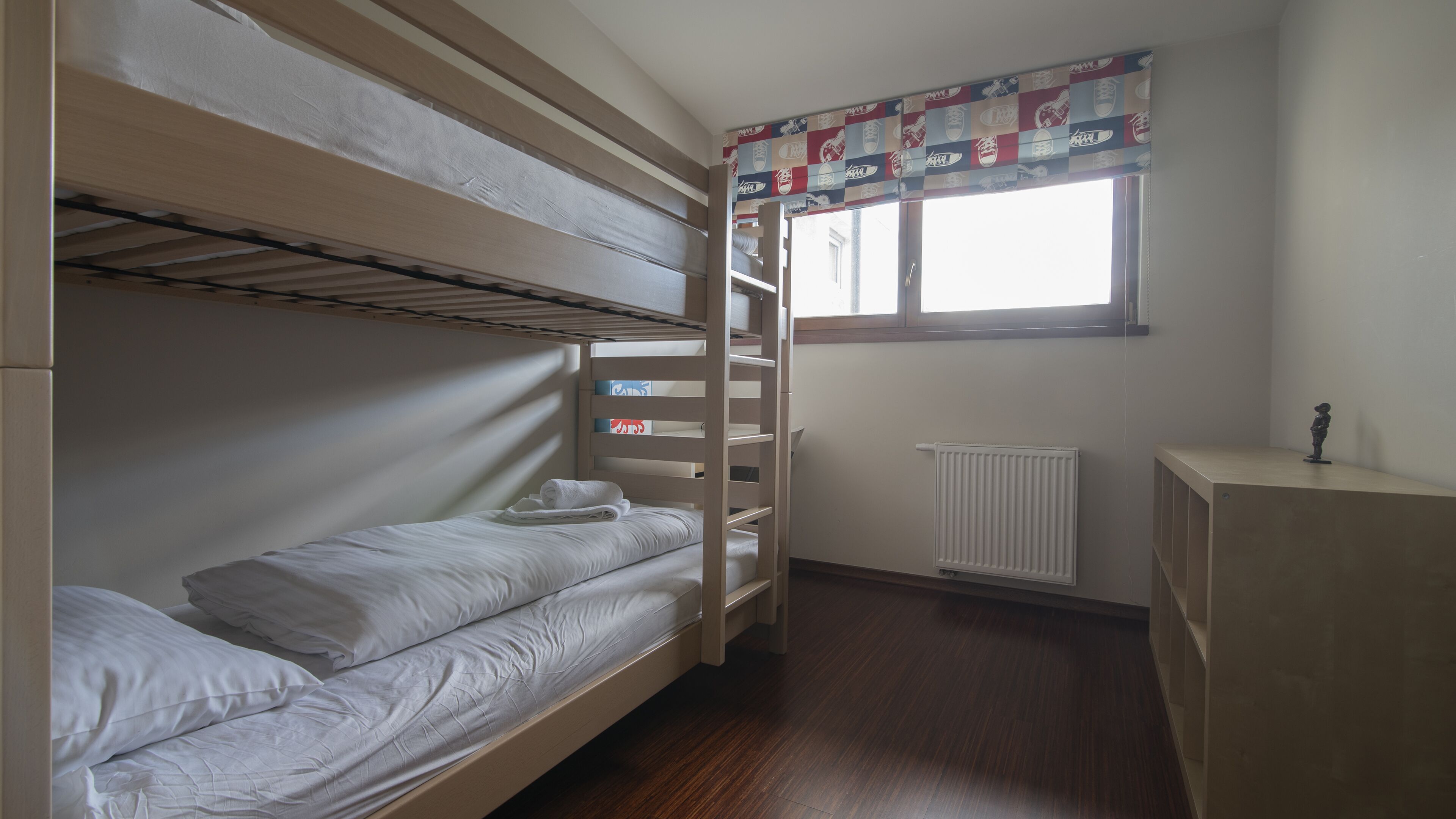 A bunk bed room with a window, radiator, and a small cabinet.