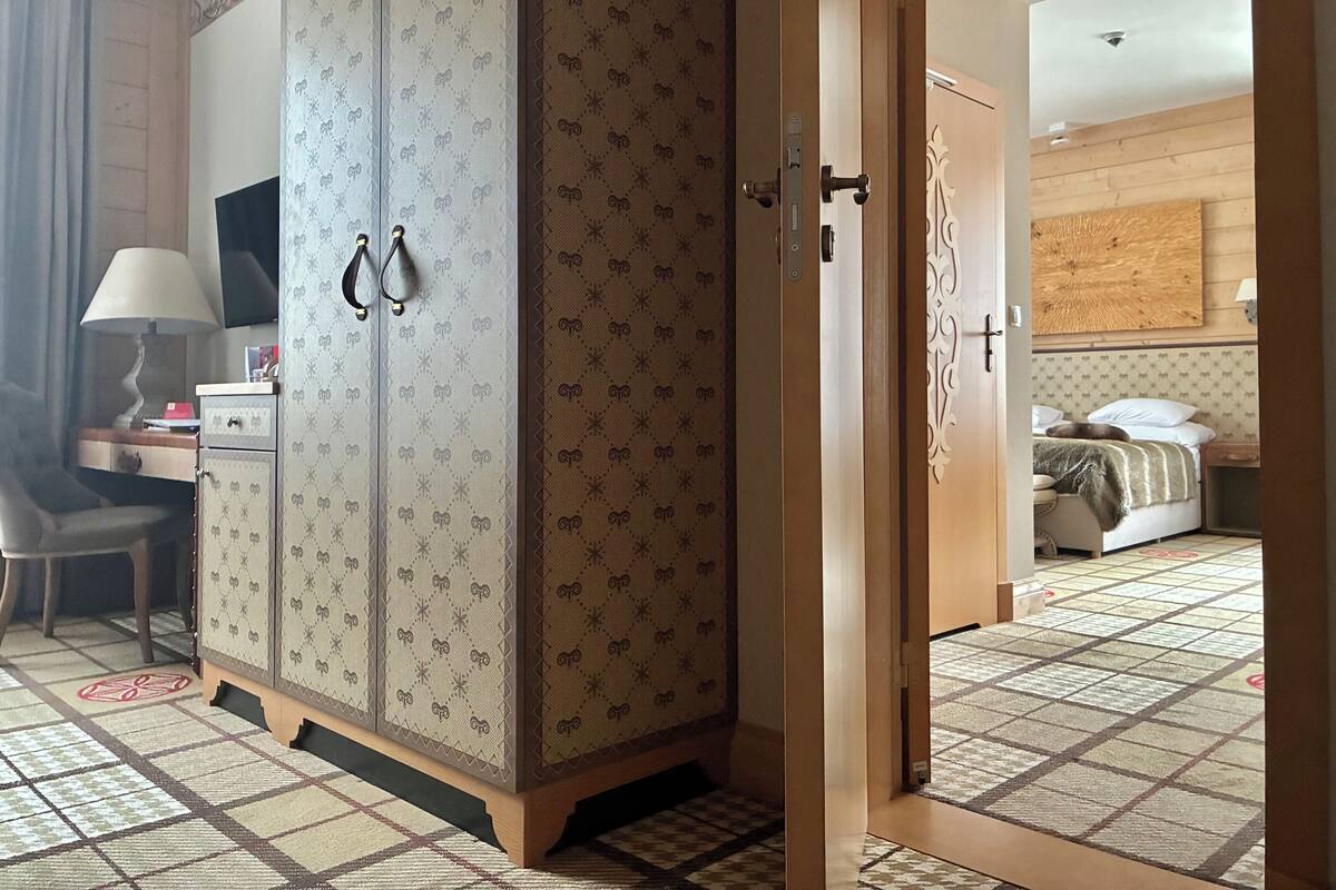 Una habitación de hotel con un armario, un escritorio con lámpara, una cama y un suelo estampado.