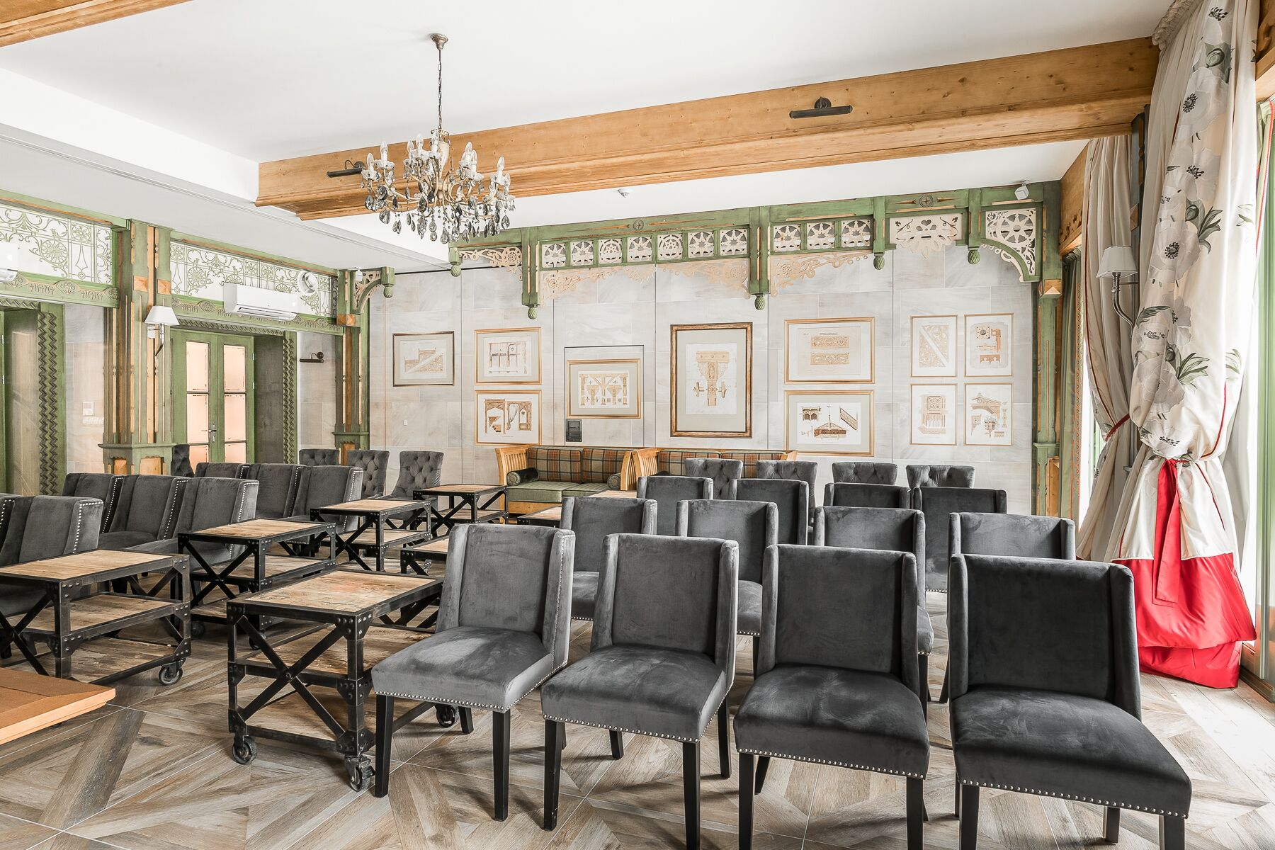 A spacious room with multiple seating areas, a chandelier, and framed architectural drawings on the walls.