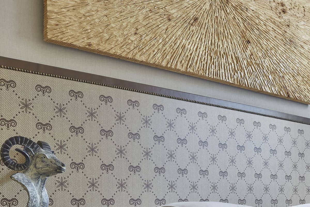 Un dormitorio con un cabecero estampado, una escultura decorativa de cabeza de carnero, una mesita de noche y una manta de piel sobre la cama.
