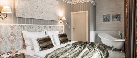 A bedroom with a large bed, a nightstand, a wall-mounted lamp, a decorative headboard, a large mirror, and a bathtub.