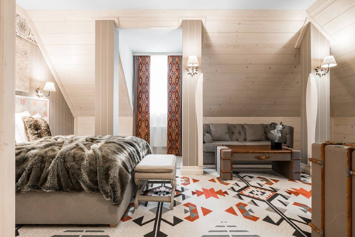 Una habitación acogedora y bien iluminada con una cama grande, un sofá y una mesita. Hay cortinas y una lámpara en la pared.