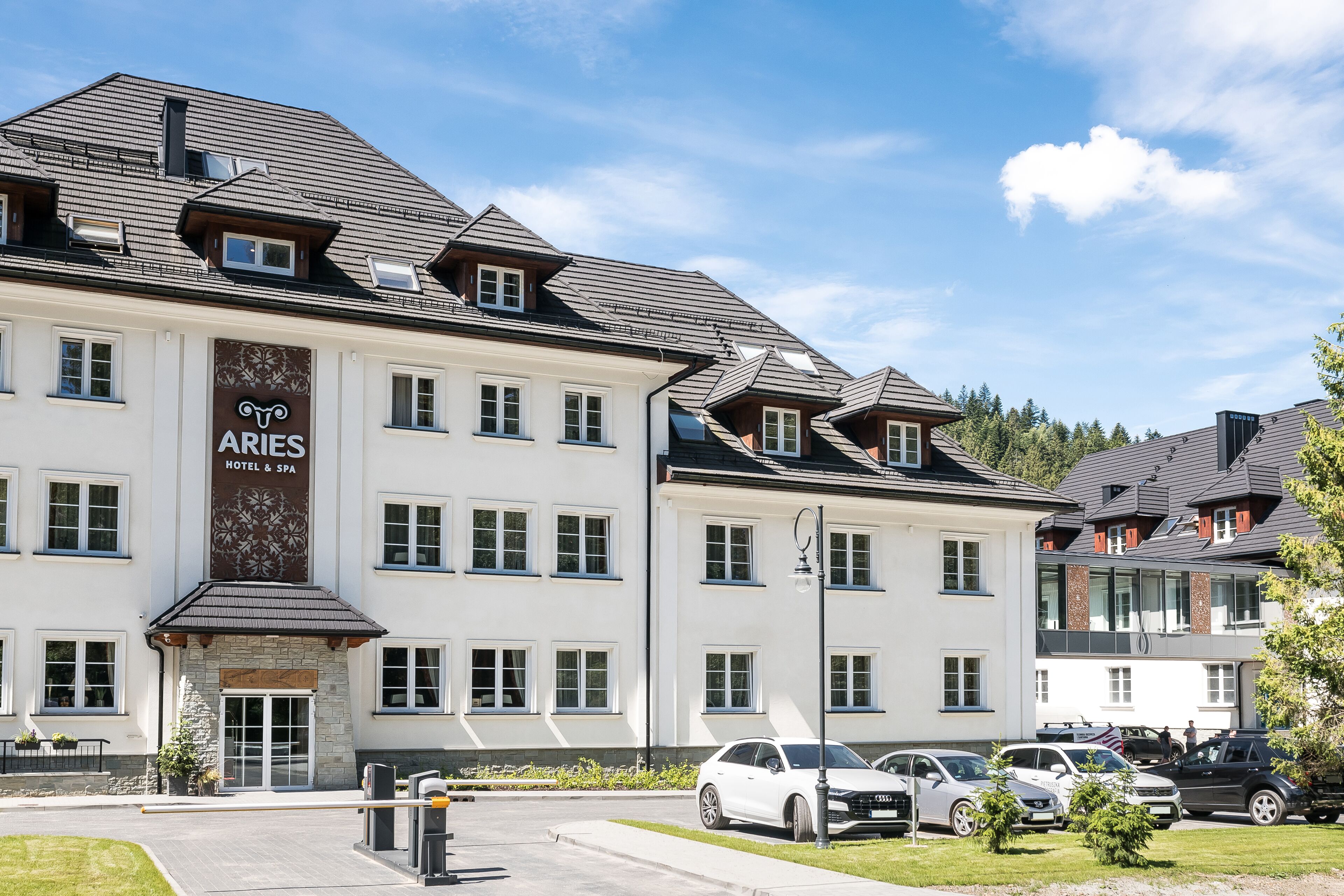 A hotel with a prominent sign, multiple windows, and parked cars in front.
