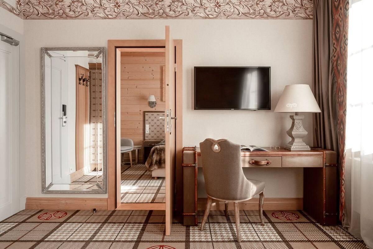 Habitación de hotel con un escritorio de madera, una silla, un televisor, un espejo y un suelo estampado.
