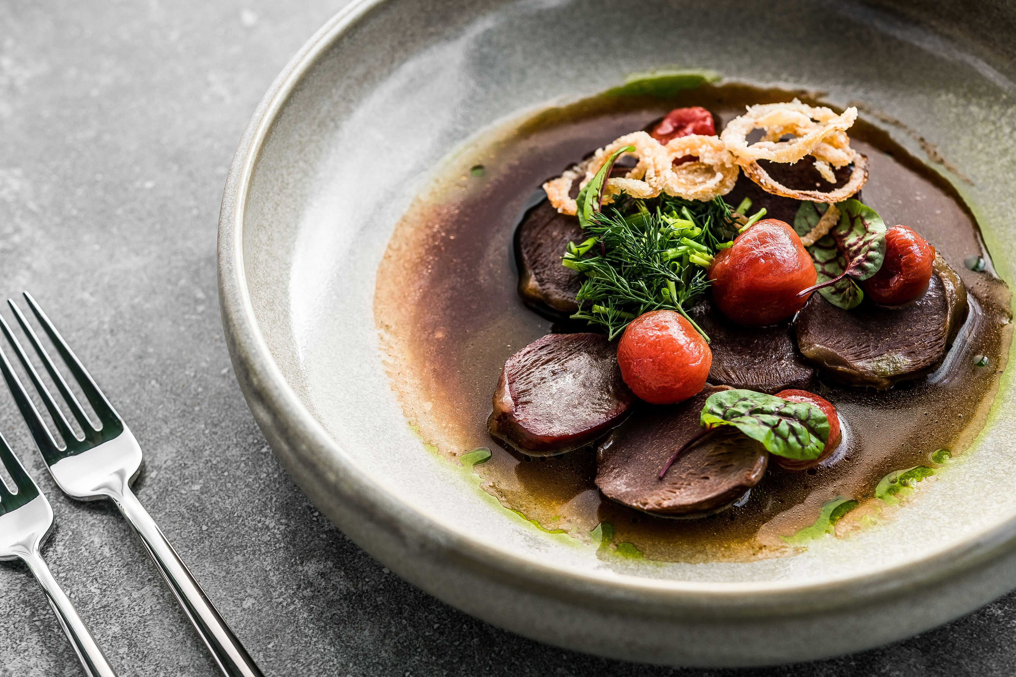 A plate of food with sliced meat, cherry tomatoes, and greens.