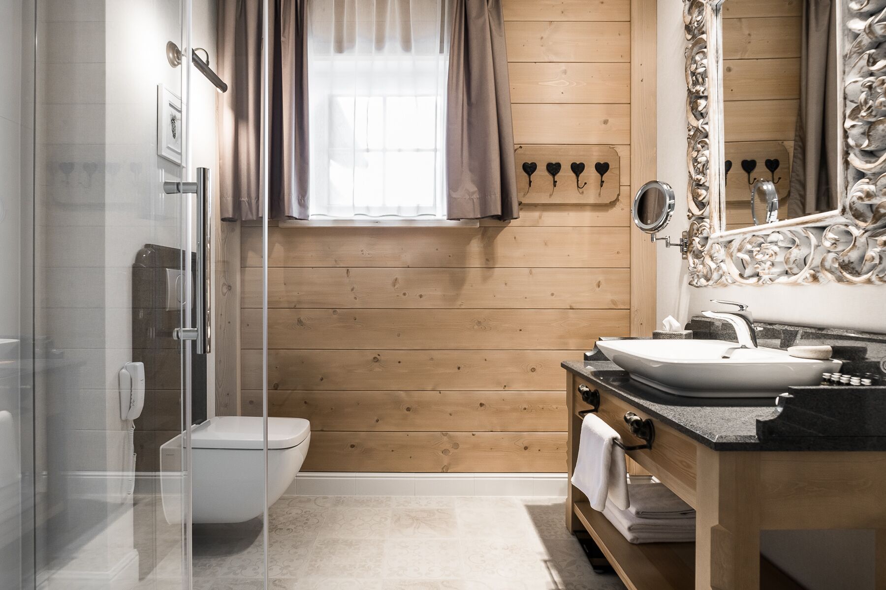 A modern bathroom with a glass shower enclosure, a toilet, a sink with a vanity, and a large mirror with ornate detailing.