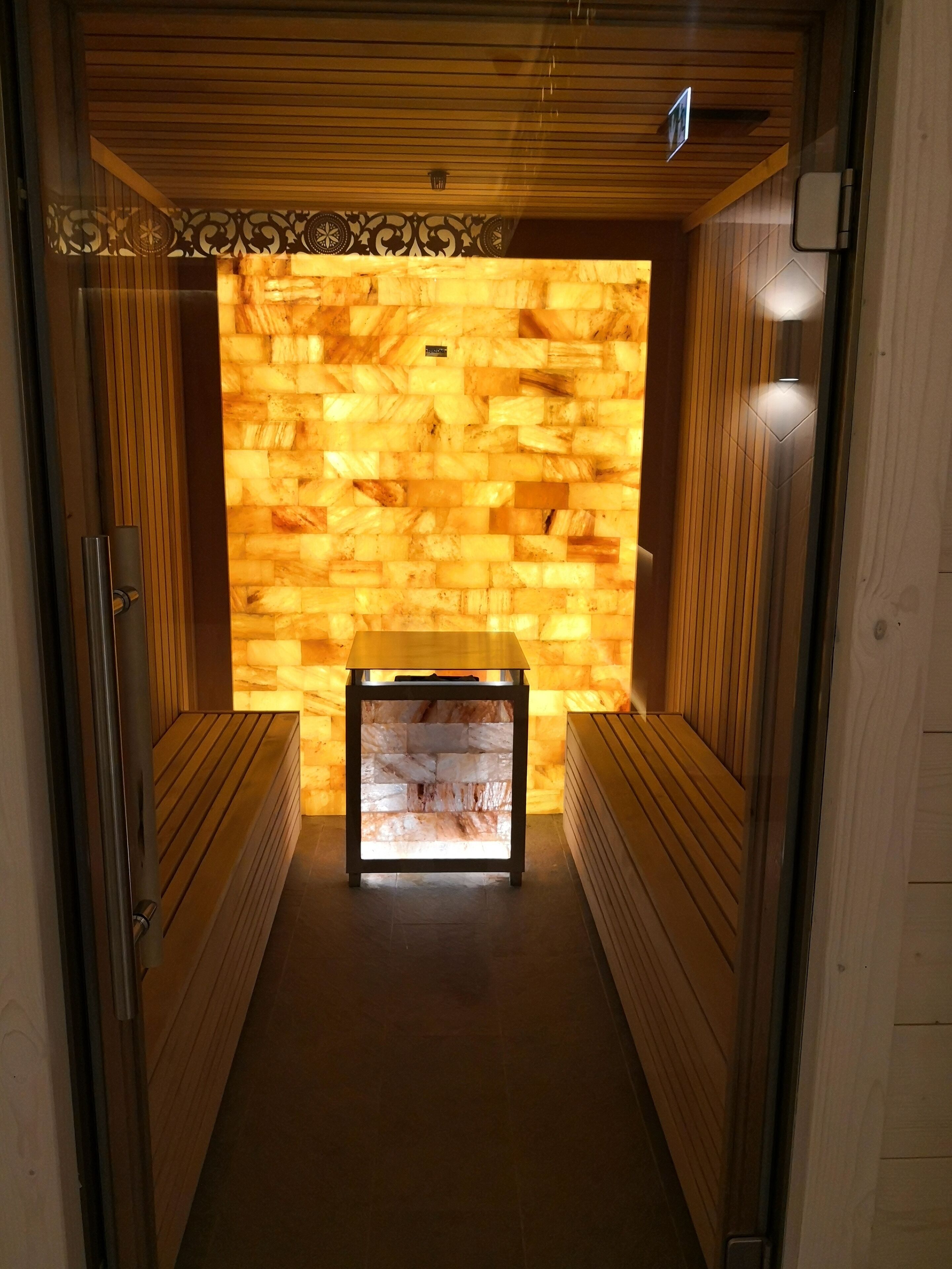 A sauna room with wooden benches, a central bench, and a stone wall.