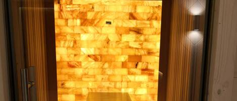 A sauna room with wooden benches, a central bench, and a stone wall.