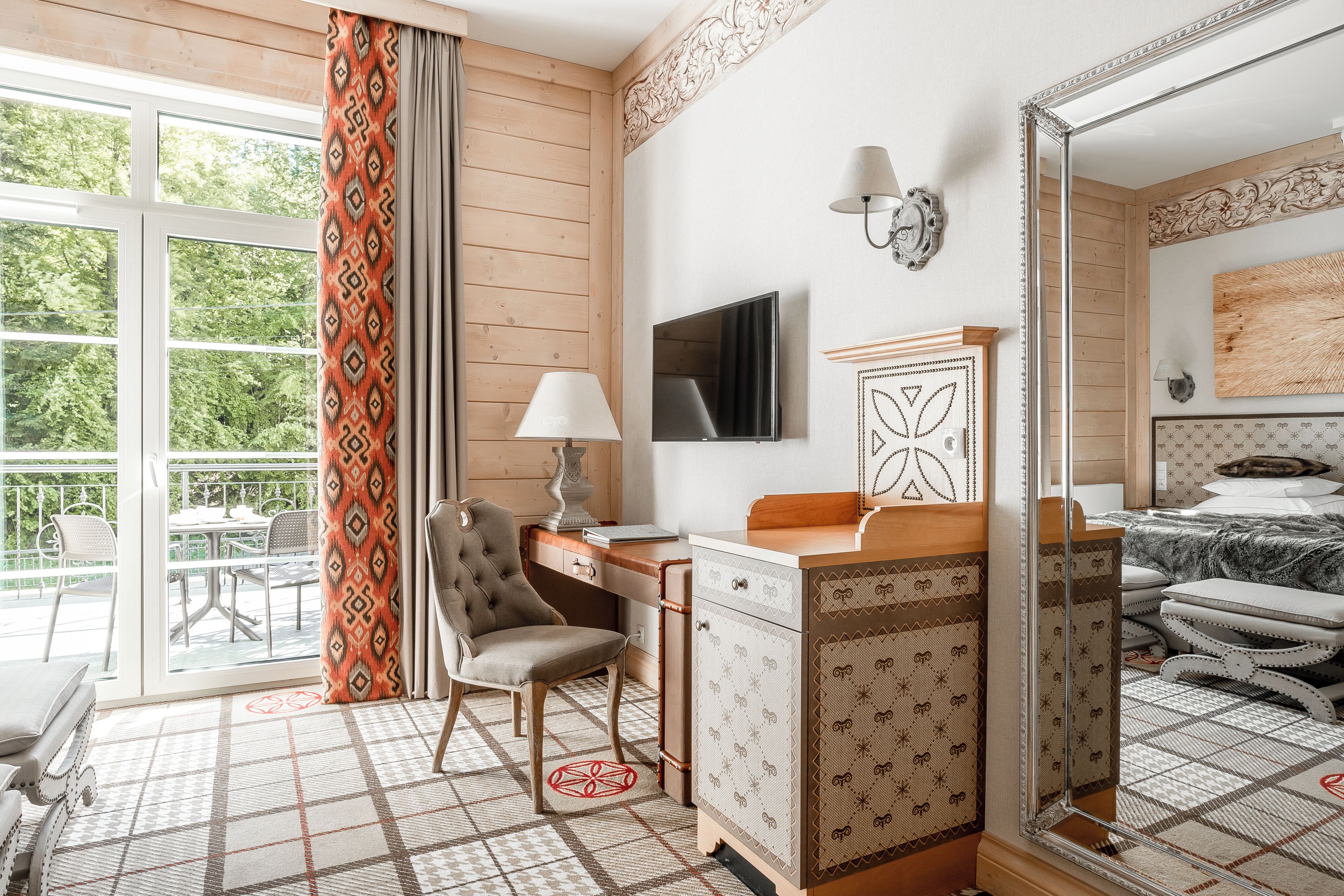 A hotel room with a desk, chair, and a large mirror.