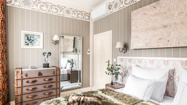 A bedroom with striped wallpaper, a large mirror, a wooden dresser, a bed with white bedding, and a decorative wall piece. - Aries Hotel & SPA Wisla (Wisla)
