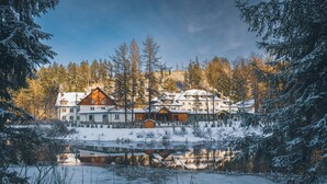 A large lodge with multiple buildings, a reflective pond, and a forested backdrop. - Aries Hotel & SPA Wisla (Wisla)