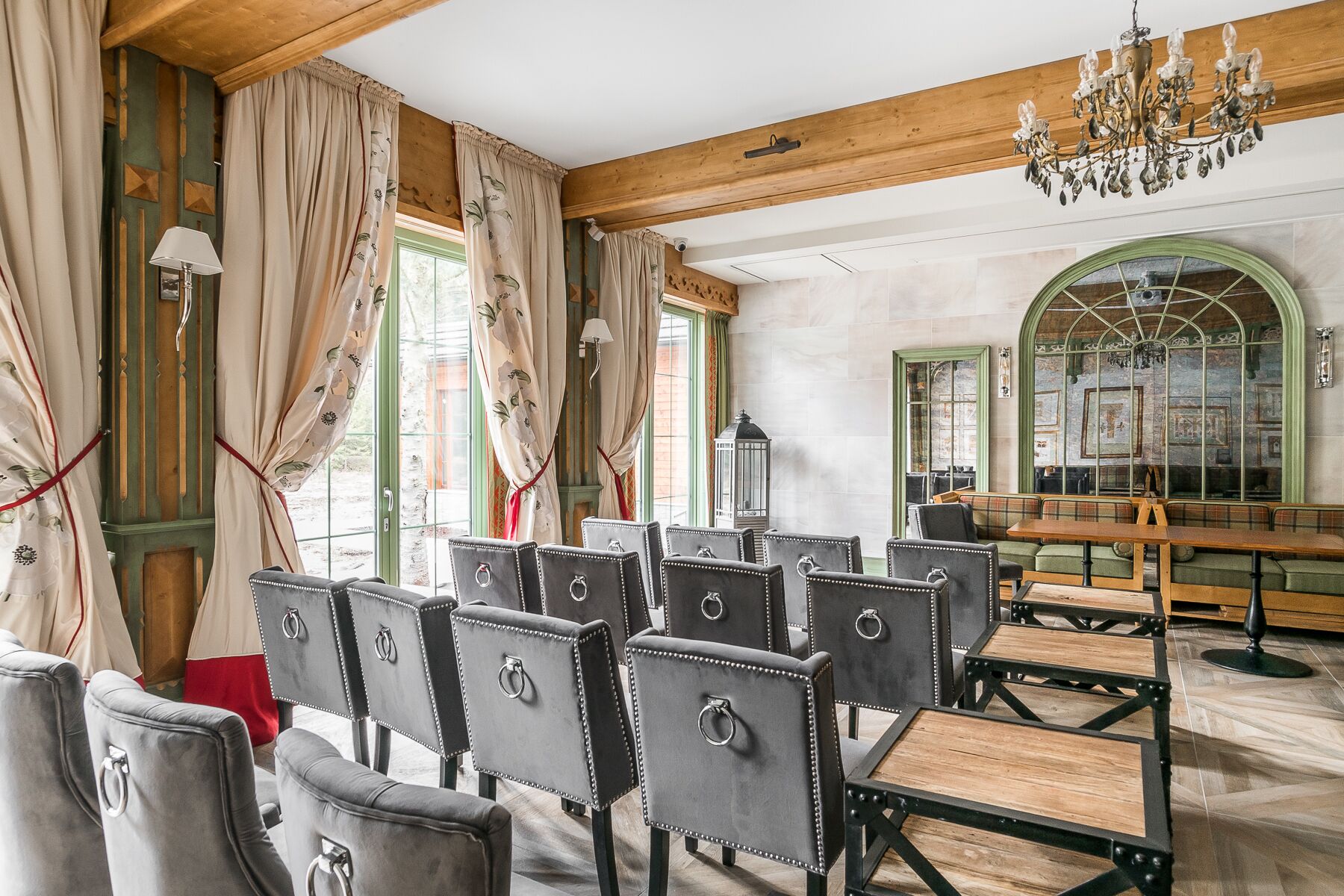 A room with wooden beams, a chandelier, and a seating area with cushioned chairs and tables.