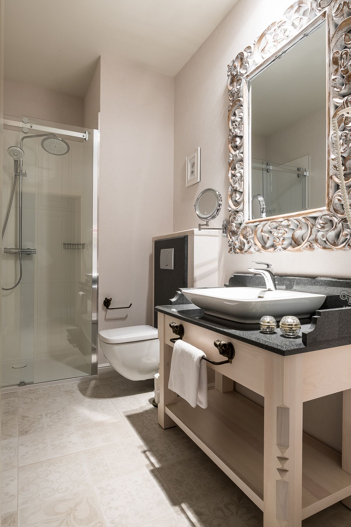 Ein Badezimmer mit Glasdusche, Toilette, Waschbecken mit dekorativem Spiegel und Handtuchhalter.