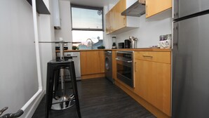 Eine kleine Küche mit Holzschränken, einem Edelstahlkühlschrank, einer Waschmaschine und einer Kaffeemaschine.