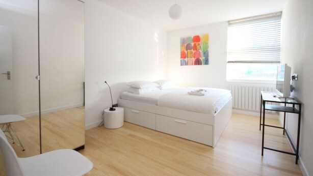 Ein modernes Schlafzimmer mit Bett, Nachttisch und einem Fenster mit Jalousien.